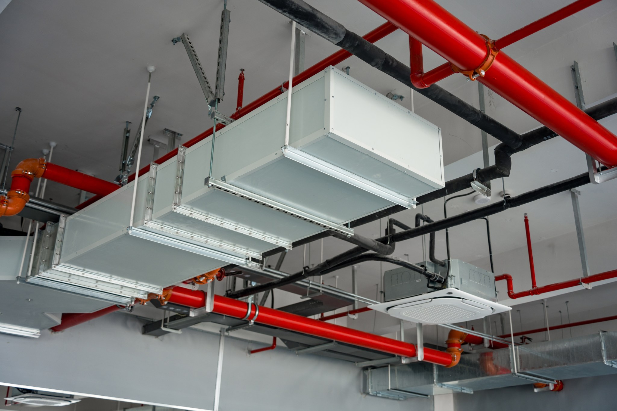 Tuyauterie de gicleurs rouge coordonnée avec les conduits de ventilation dans un plénum de plafond